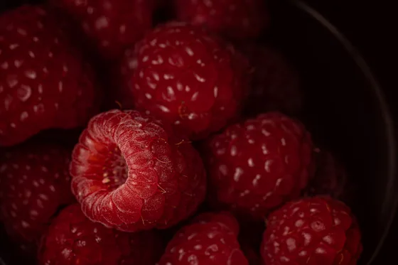 Raspberries filling a dark bowl, lit from one side