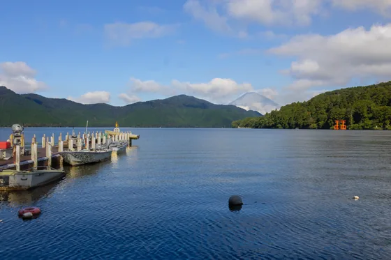 A pier reaching into the lake, hills and a red torii beyond