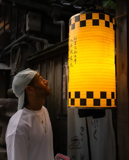 A man looking up at a large yellow paper lantern in an alley
