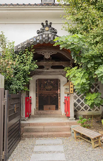 A small shrine gate set into a wall, overgrown with green