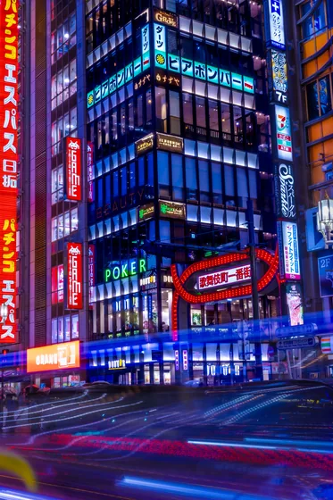 Neon stacked up the face of a tower at the Kabukichō gate, traffic drawn into light trails below